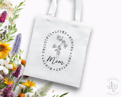 Celebrate mom with our Mom Tote Bag! Featuring a simple yet elegant design, this bag is perfect for Mother's Day. The line-drawn flowers and heartfelt words such as "beautiful", "loved", and "strong" make this tote both stylish and meaningful.