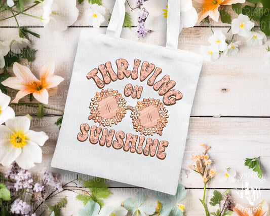 Featuring sunglasses bordered with vibrant flowers and the uplifting phrase "thriving on sunshine", this bag is the perfect accessory for spring.